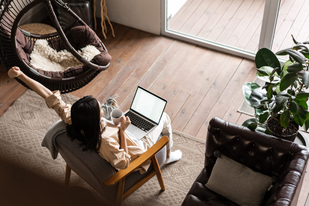 Vrouw die thuis aan het werk is met de laptop op schoot genietend van haar kofie